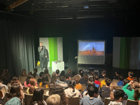 Dr. Christian Klepp hält einen Vortrag in einem Theaterraum vor einer Schulklasse 